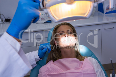 Woman lying on dentist chair while dentist adjusting electric lamp