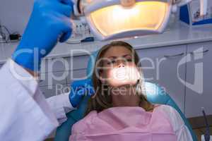Woman lying on dentist chair while dentist adjusting electric lamp