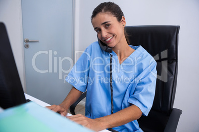 Portrait of doctor talking on phone while working on computer