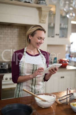 Woman using digital tablet while preparing cookies