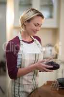 Smiling woman holding bowl of dried blue berries in kitchen