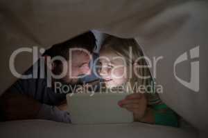 Father and daughter lying under blanket and using digital tablet