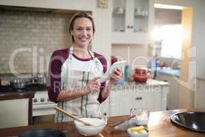 Woman using digital tablet while preparing cookies in kitchen