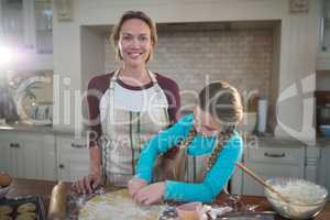 Smiling mother and daughter preparing cookies in kitchen