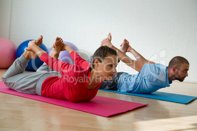 Student practicing bow pose with instructor in yoga studio