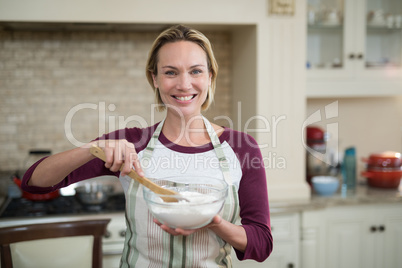 Smiling woman mixing eggs and wheat flour in a bowl
