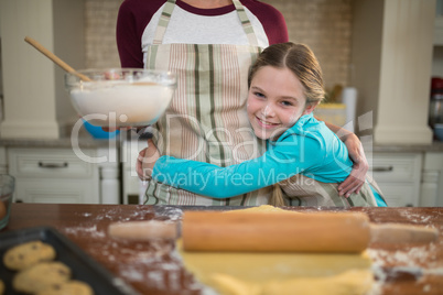 Daughter hugging mother while preparing cookies in kitchen