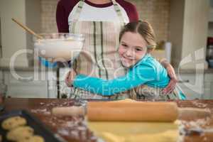 Daughter hugging mother while preparing cookies in kitchen