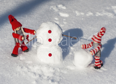 wooden dolls in red knitted clothes roll down snowballs to buil