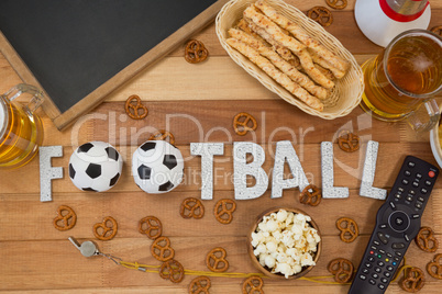Remote control, slate, snacks, drinks and football word arranged on table