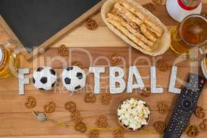 Remote control, slate, snacks, drinks and football word arranged on table