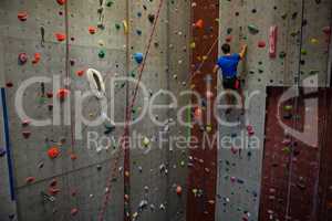 Rear view of athlete climbing wall in club