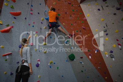 Woman instructing athlete in climbing wall at health club