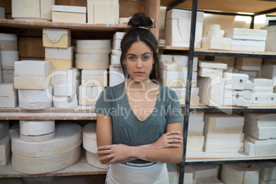 Female potter standing with arms crossed in pottery workshop