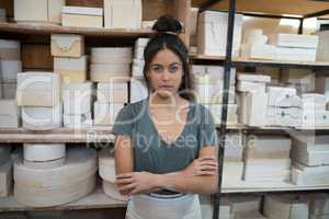 Female potter standing with arms crossed in pottery workshop