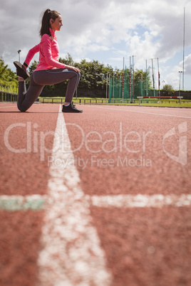 Woman performing stretching exercise on a race track