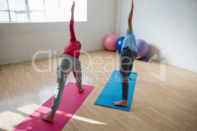 Instructor with female student practicing triangel pose in yoga studio