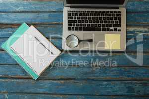 Blank book, pen, magnifying glass and laptop on wooden plank