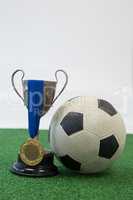 Football, trophy and medal on artificial grass against white background