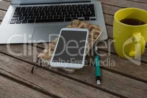 Laptop, mobile phone, dairy, pen and coffee on wooden plank