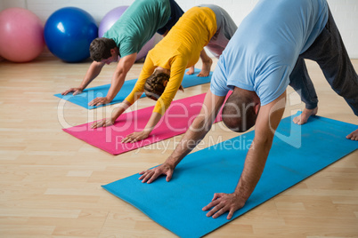 Instructor guiding students in practicing downward facing dog pose at yoga studio