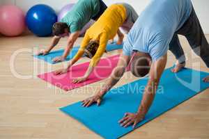 Instructor guiding students in practicing downward facing dog pose at yoga studio