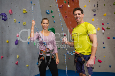 Portrait of athletes holding rope while standing by climbing wall
