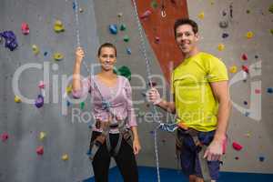 Portrait of athletes holding rope while standing by climbing wall