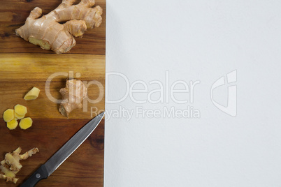Directly above view of fresh chopped ginger with knife on wooden cutting board