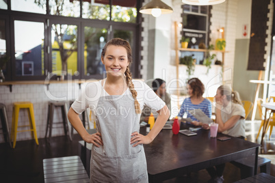 Portrait of smiling young waitress with hands on hip at cafe