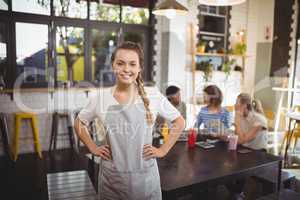 Portrait of smiling young waitress with hands on hip at cafe
