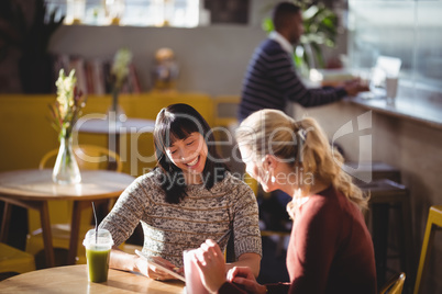 Smiling female friends using tablet computer at coffee shop