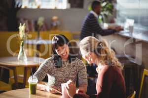 Smiling female friends using tablet computer at coffee shop