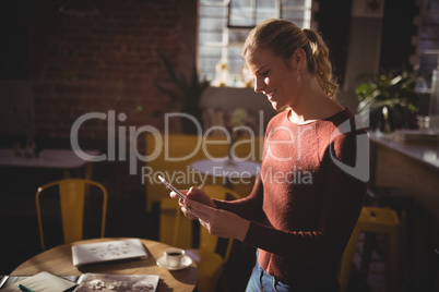 Smiling young blond woman using smartphone at coffee shop
