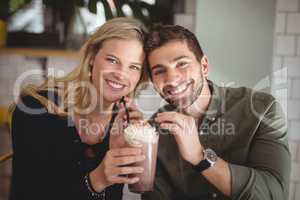 Smiling young couple holding fresh dessert at coffee shop