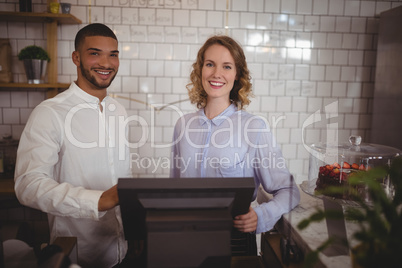 Portrait of smiling waitress and male owner standing by computer