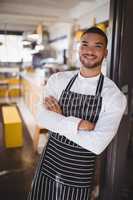Portrait of handsome young waiter standing with arms crossed