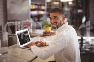 Portrait of smiling young male owner sitting with laptop at counter