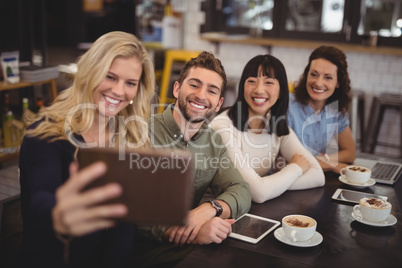 Young woman taking selfie with friends from tablet at cafe