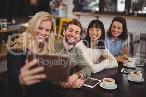 Young woman taking selfie with friends from tablet at cafe