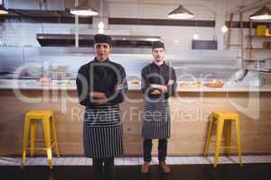 Portrait of confident young wait staff standing with arms crossed against counter