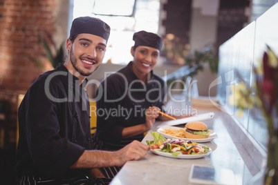 Portrait of smiling young wait staff sitting with food and clipboard at counter