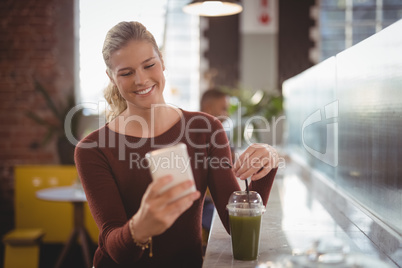 Smiling young blond woman using smartphone while sitting with drink at counter Smiling young blond woman using smartphone while sitting with drink at counter