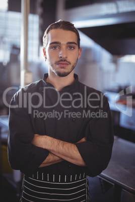 Portrait of confident young male barista standing with arms crossed