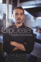 Portrait of confident young male barista standing with arms crossed