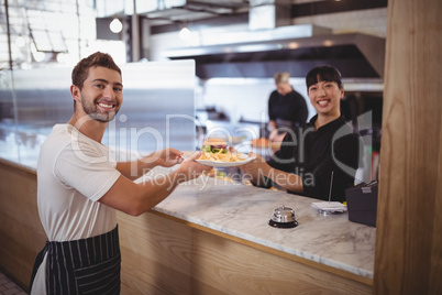 Portrait of smiling female chef and waiter holding plate at counter
