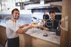 Portrait of smiling female chef and waiter holding plate at counter