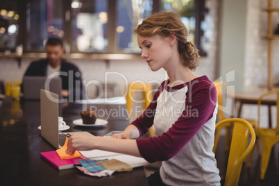 Confident female designer sitting with notebooks and papers at coffee shop