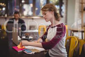 Confident female designer sitting with notebooks and papers at coffee shop