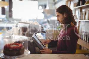 Side view of young waiter using cash register at coffee shop